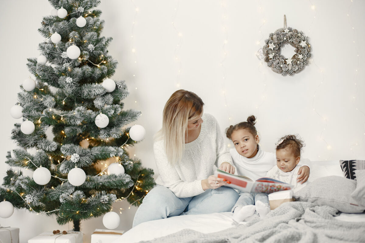 美国人们在为圣诞节做准备母亲在和女儿们玩耍一家人在节日的房间里休息孩子穿着毛衣传统混合肖像