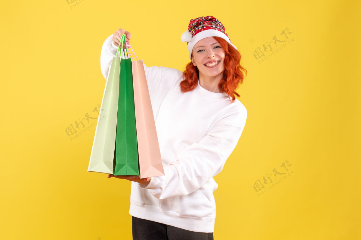 节日黄色墙壁上拿着购物包裹的年轻女子的正视图情感圣诞节包