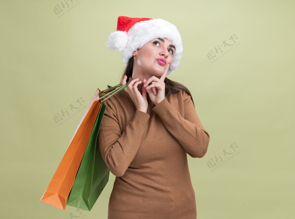 圣诞节年轻漂亮的女孩戴着圣诞帽 肩上挎着礼品袋 孤零零地站在橄榄绿的墙上橄榄年轻印象深刻