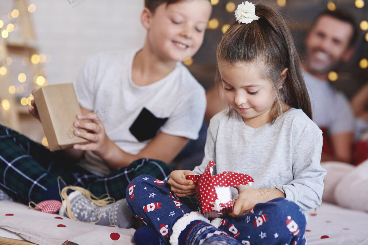 卧室可爱的女孩在床上打开圣诞礼物圣诞树家庭欢快