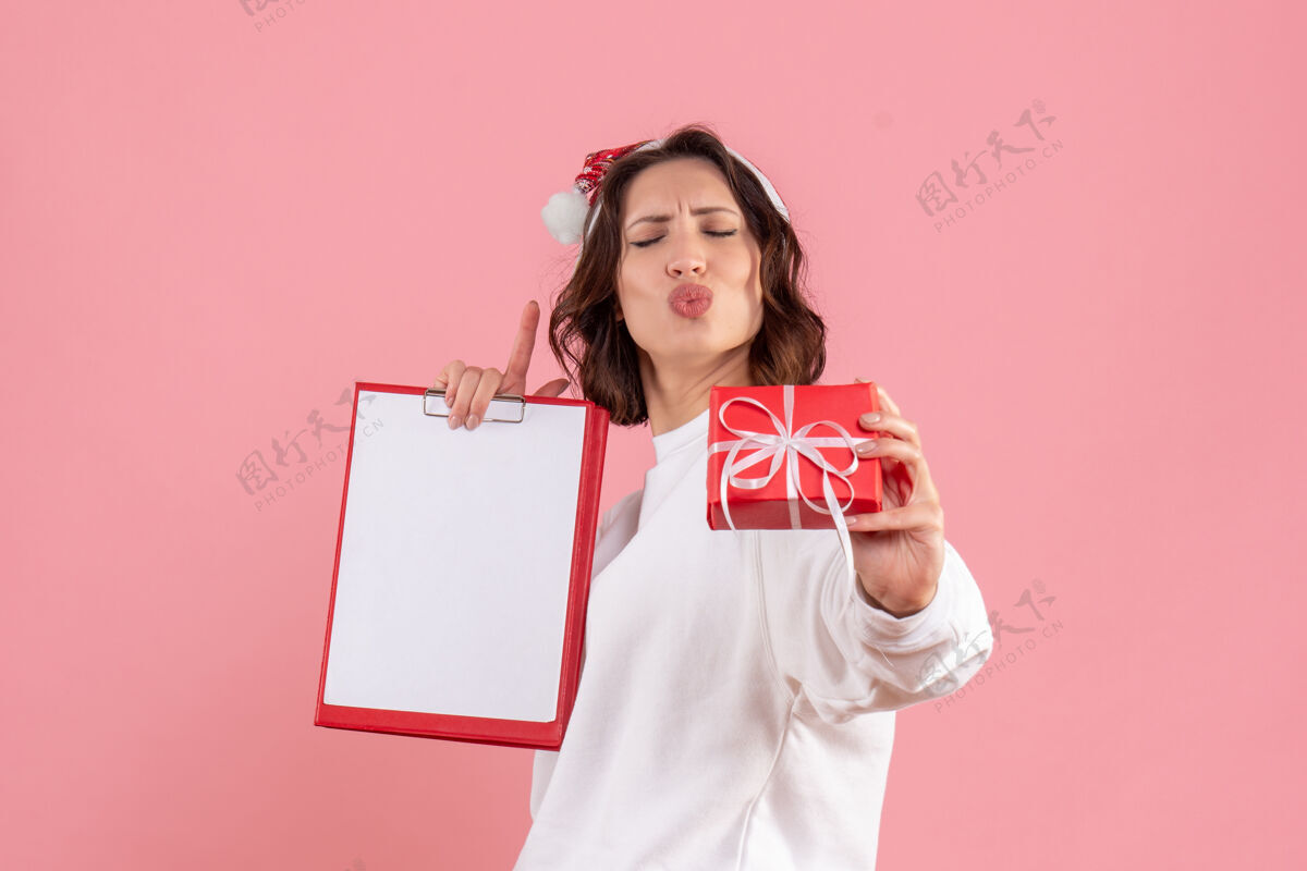 年轻的女性前视图的年轻女子举行小圣诞礼物和文件说明在粉红色的墙上小圣诞节前面