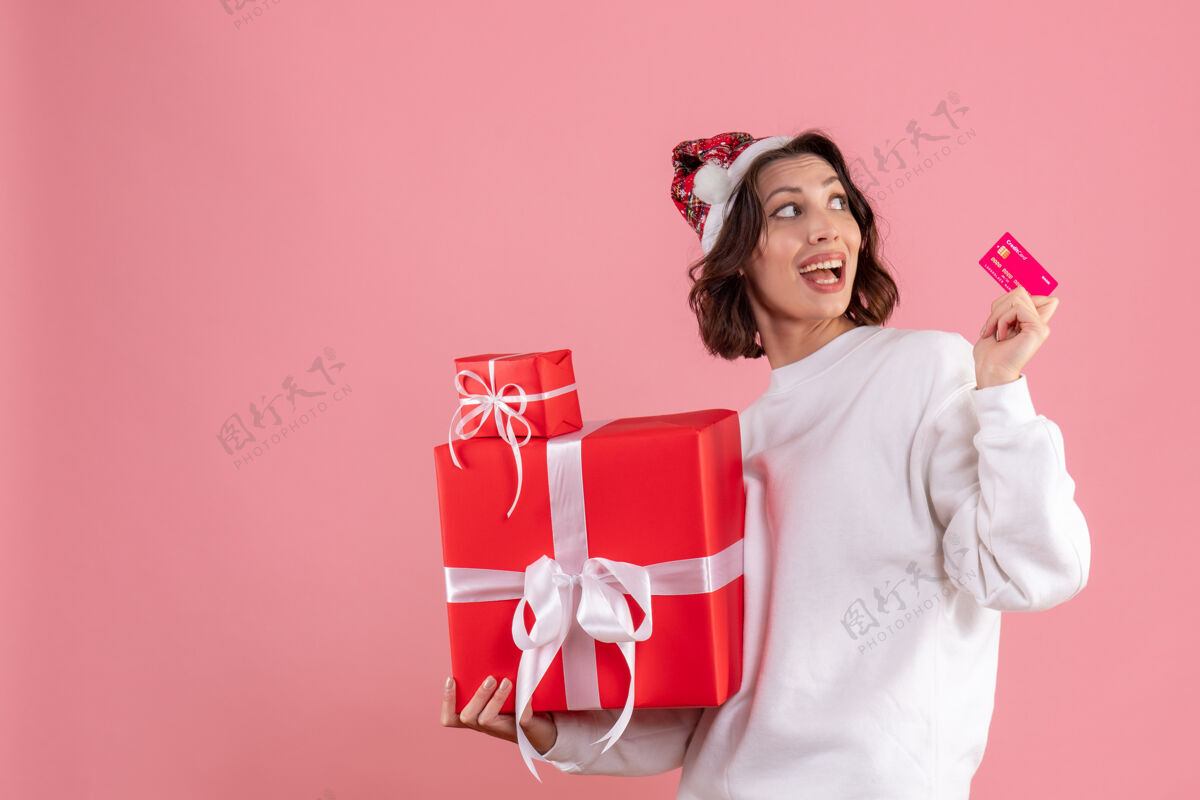 情感粉红色墙上手持圣诞礼物和银行卡的年轻女子的正视图女人节日年轻的女人