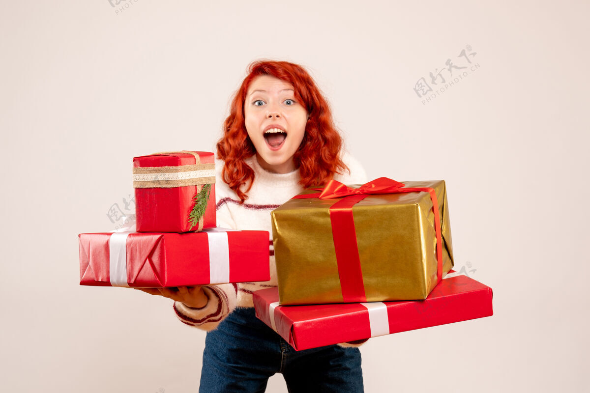 节日前视图的年轻女子携带圣诞礼物的白墙前面礼物盒子
