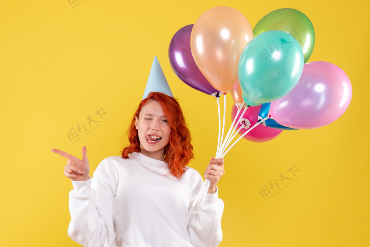 圣诞节前视图的年轻女子手持可爱的彩色气球在黄色的墙上举行情感气球