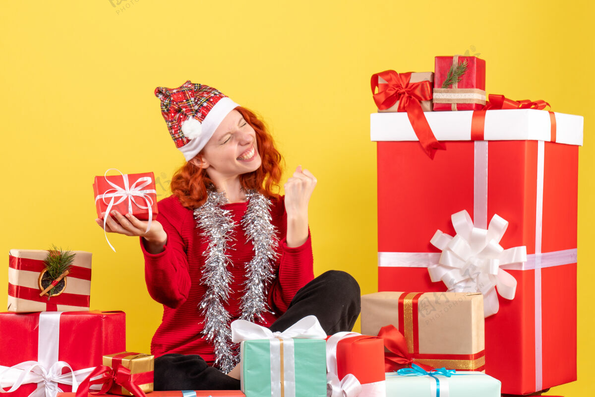 周围坐在黄色墙上的圣诞礼物周围的年轻女子的正视图衣服圣诞节情感