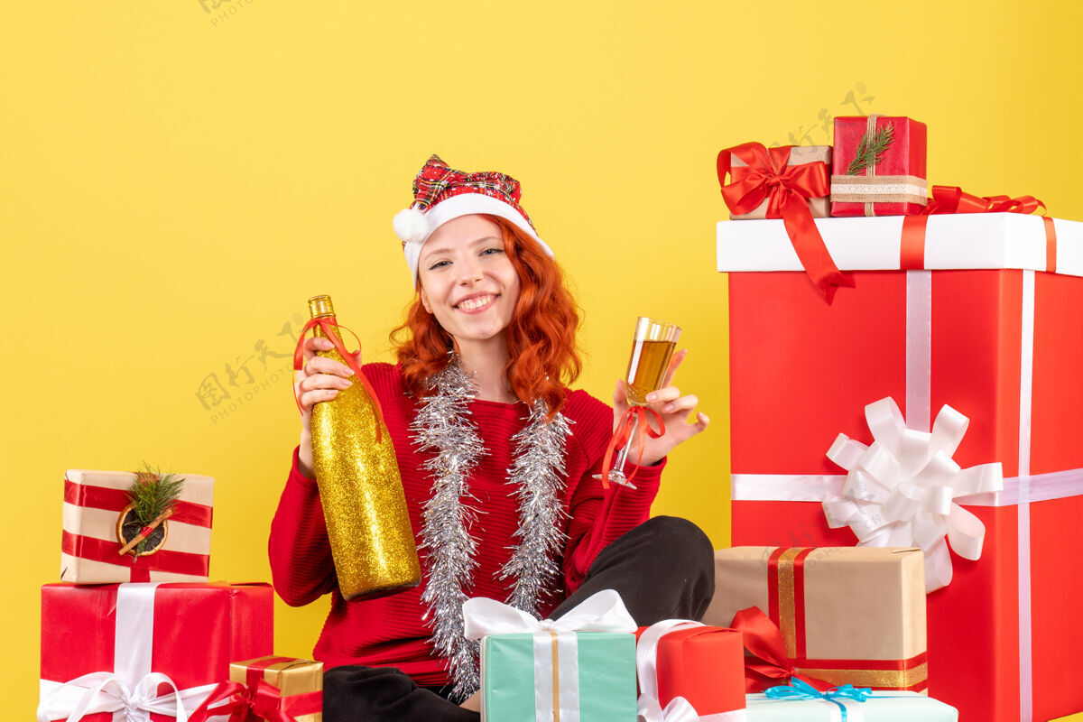 女性年轻女子围坐在圣诞礼物旁 在黄色墙壁上用香槟庆祝的正面视图前面快乐人