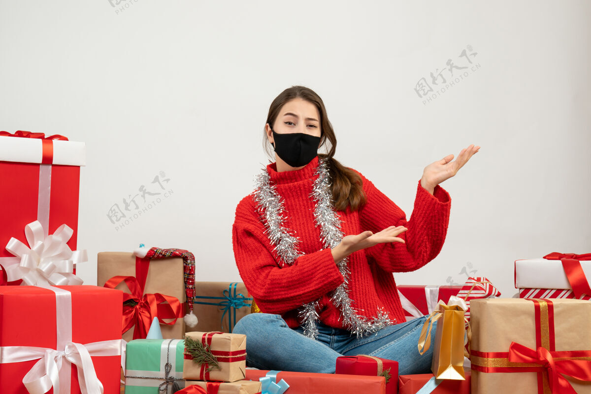 年轻女孩穿着红色毛衣 戴着黑色面具的年轻女孩 在白色的礼物上展示着坐在周围的东西东西坐着礼物