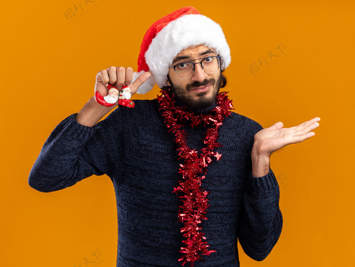 手年轻帅哥戴着圣诞帽 脖子上戴着花环 手里拿着玩具 手被隔离在橙色的背景上年轻未发布帅气