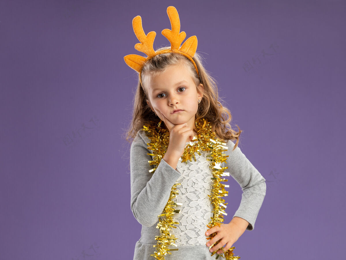 小想着那个戴着圣诞发箍的小女孩 脖子上戴着花环 手指放在脸颊上 手放在臀部 在蓝色背景上与世隔绝头发圣诞节箍