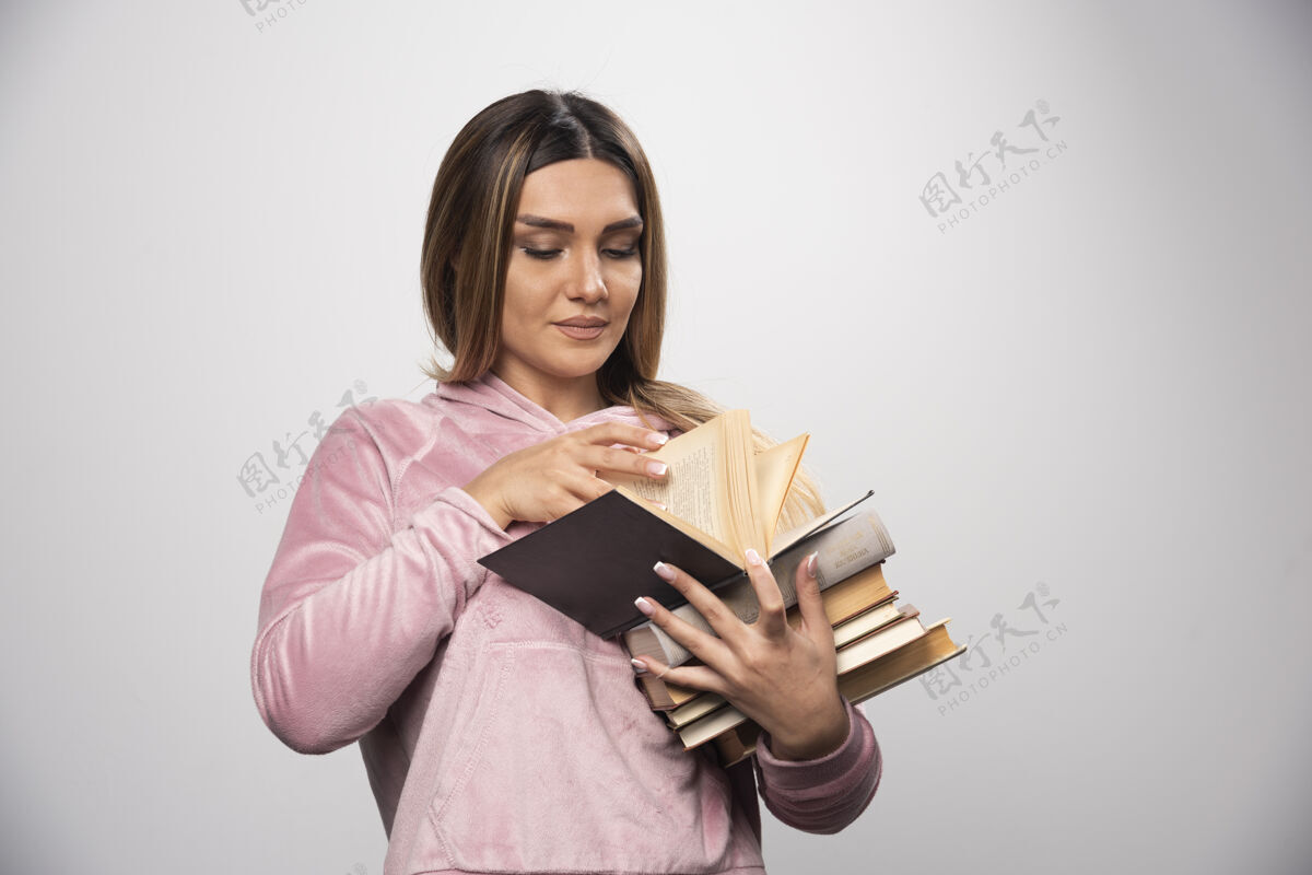 摆姿势一个穿着粉色衬衫的女孩手里拿着一堆书 打开上面的一本读着学生聪明学习