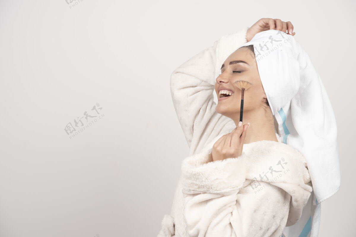 清洁一个穿着浴衣拿着化妆刷的年轻女人肖像女人浴袍