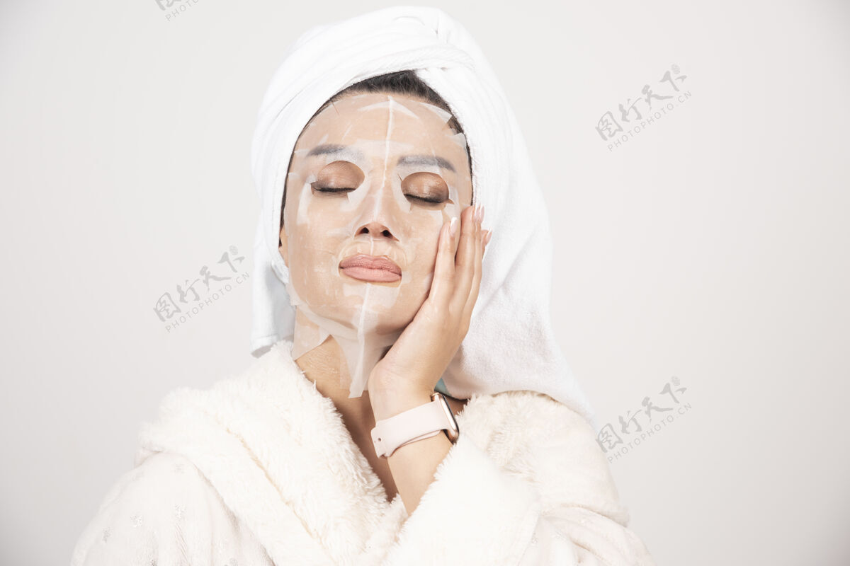 漂亮穿着浴衣 头戴毛巾的年轻女士的肖像 同时用面罩触摸她的脸女士水疗清晰
