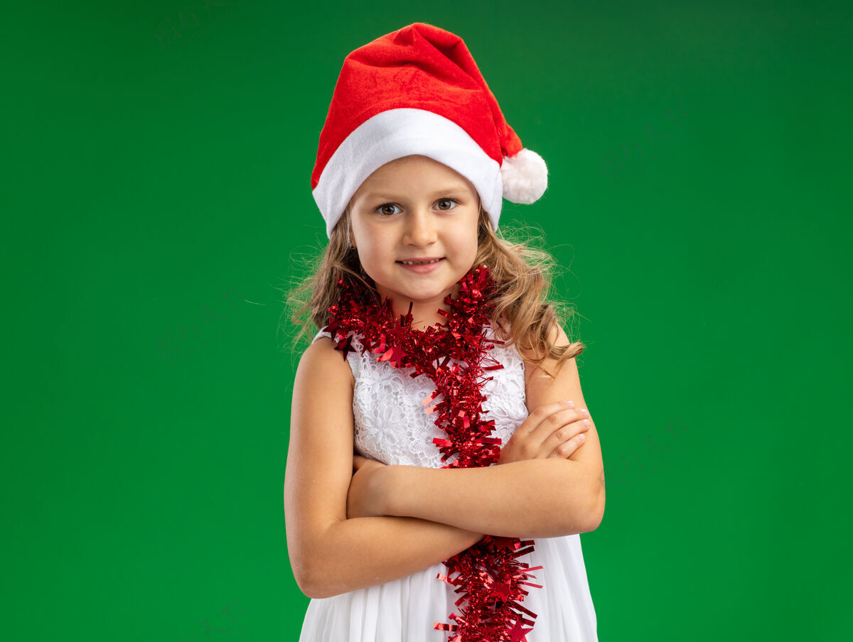 女孩微笑的小女孩戴着圣诞帽 脖子上戴着花环 双手交叉 在绿色背景下与世隔绝脖子花环圣诞节
