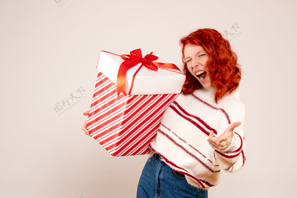 快乐白墙上拿着大礼物的年轻女子的正视图圣诞节女性前面