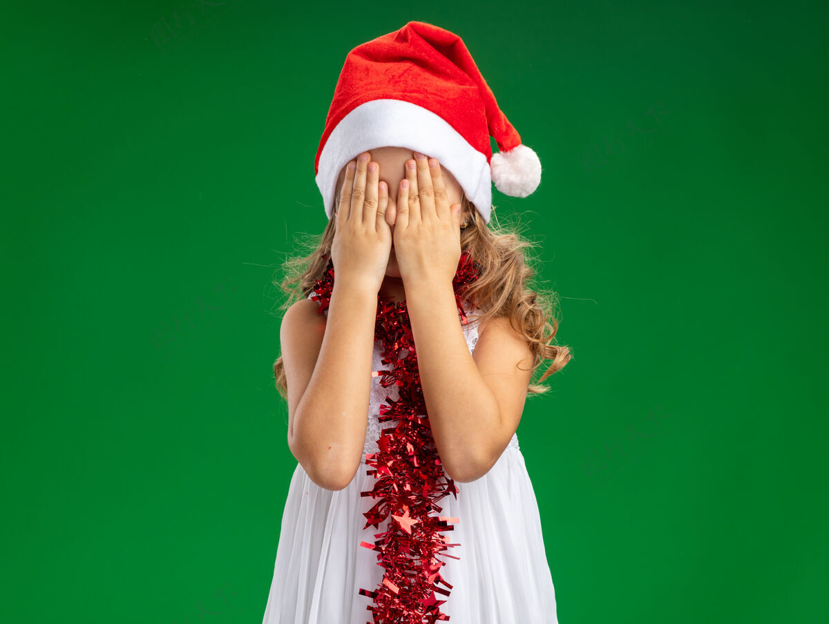 脖子小女孩戴着圣诞帽 脖子上戴着花环 手被隔离在绿色的墙上戴花环小