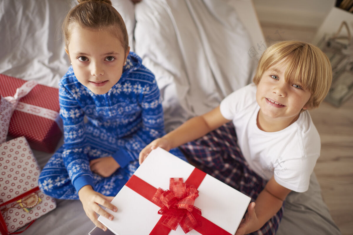 姐妹两个孩子拿着圣诞礼物坐在床上盒子节日家里室内