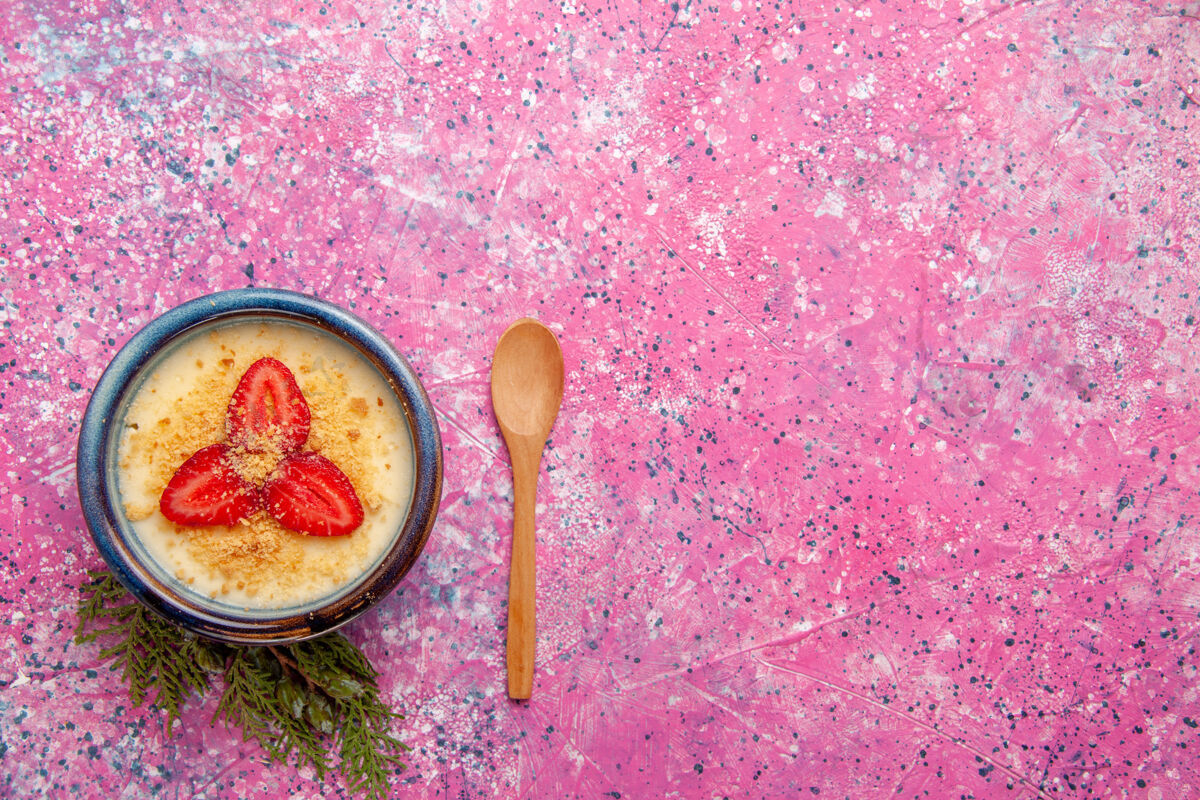 顶部顶视图美味奶油甜点 淡粉色桌面上有红色草莓片甜点冰淇淋甜水果浆果木制勺子餐具草莓