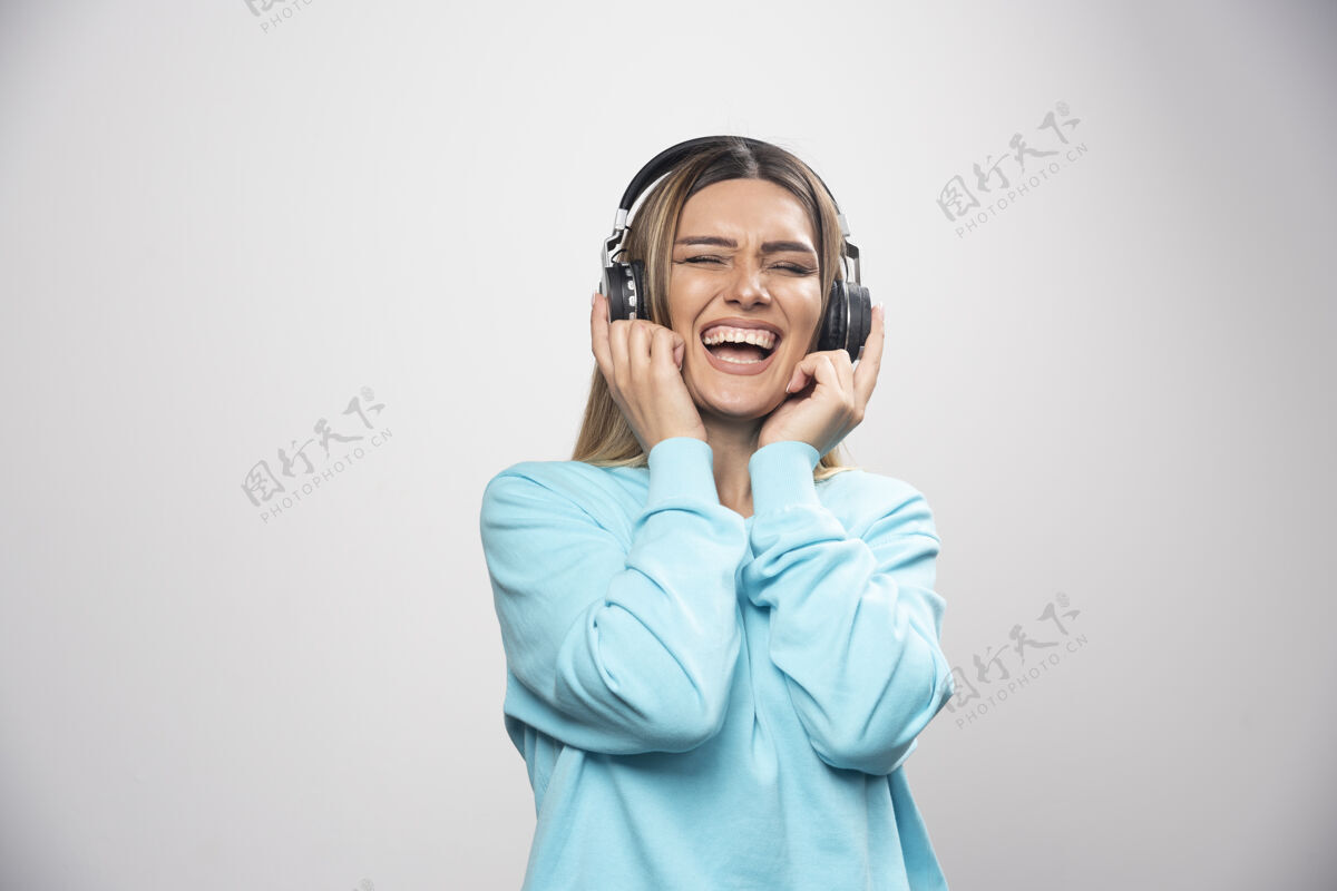 女性穿着蓝色运动衫的金发女孩戴着耳机 享受着音乐和乐趣休闲音乐快乐