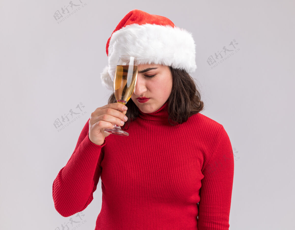 毛衣站在白色的背景下 一个穿着红色毛衣 戴着圣诞帽 手里拿着一杯香槟的年轻女孩看起来又累又无聊无聊杯子抱着