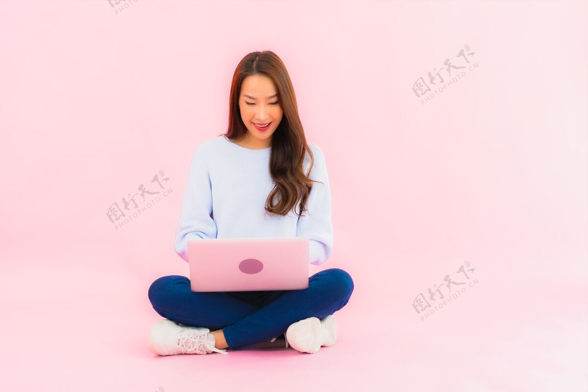 数字肖像美丽的亚洲年轻女子在粉色隔离墙上使用笔记本电脑休息室无线扶手椅