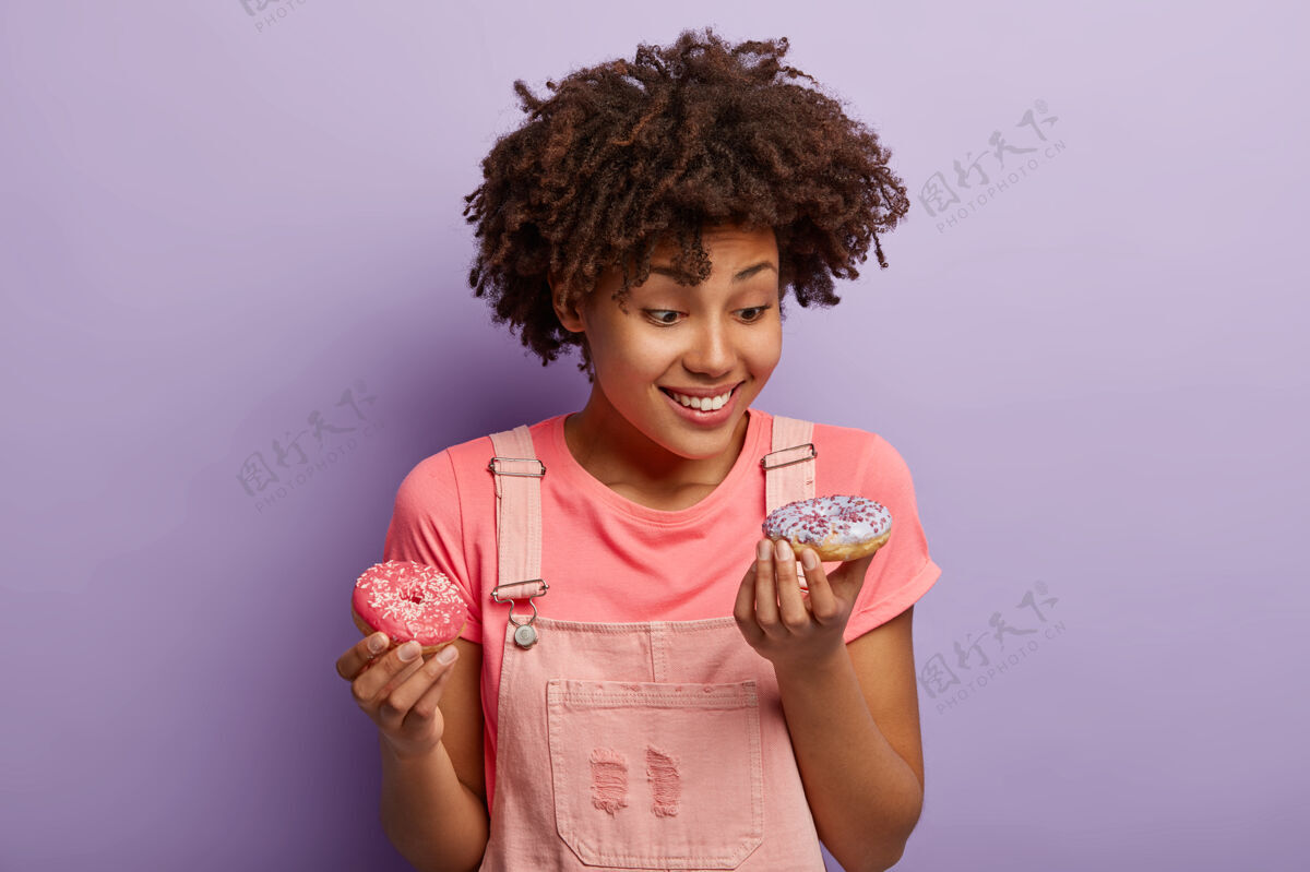 水平快乐的黑皮肤女人吃着美味的甜甜圈五颜六色工作服有趣