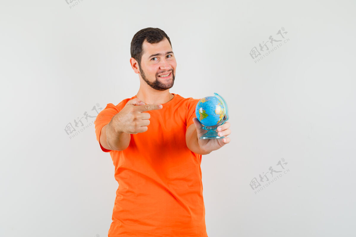 人年轻人指着世界地球仪 穿着橙色t恤 看上去很快乐 正前方的景色帅气模特衬衫