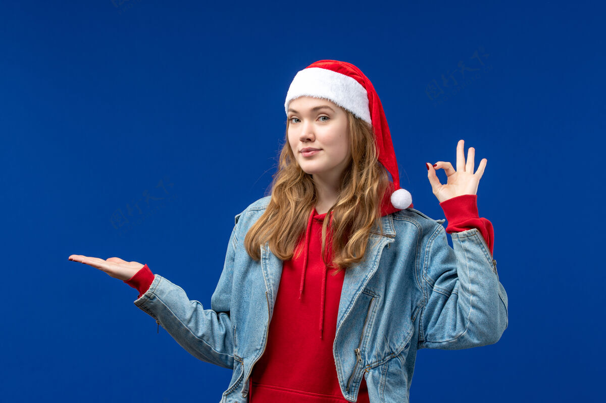 快乐正面图：戴着红色圣诞帽的年轻女性在蓝色背景上微笑着圣诞情感色彩背景微笑观点