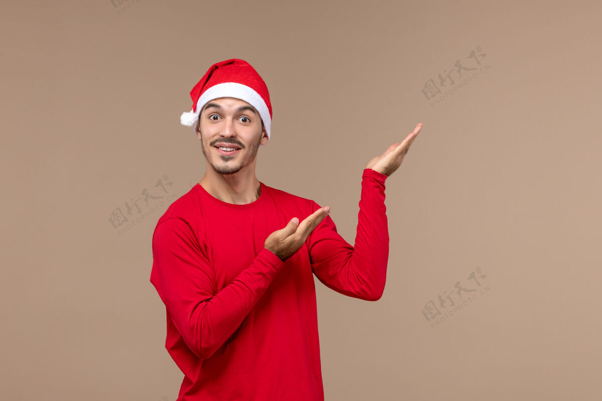欢乐正面图：年轻男性在圣诞节的棕色背景下摆出兴奋的姿势可爱快乐微笑