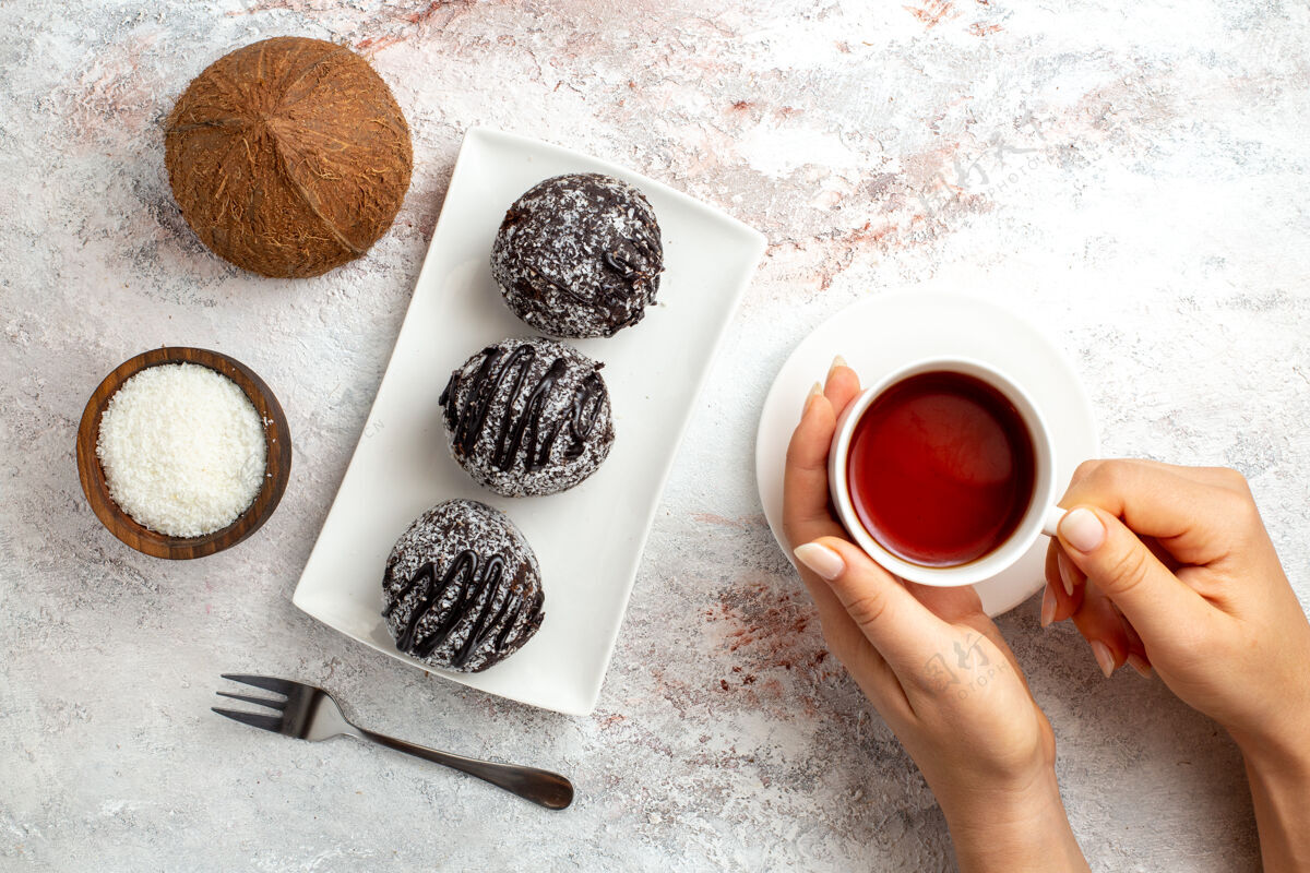 生的俯瞰巧克力蛋糕与一杯茶和椰子在白色表面巧克力蛋糕饼干糖甜饼干茶杯子视图