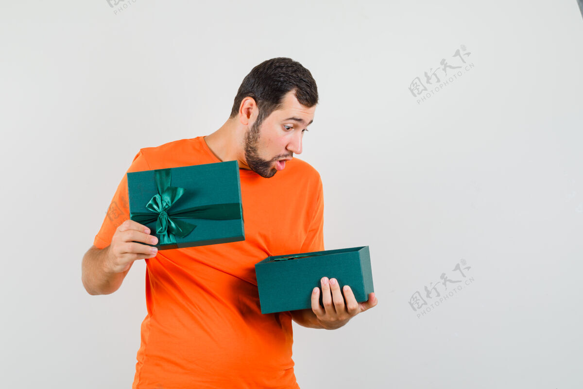 现代年轻人看着礼物盒在橙色的t恤衫和期待惊讶 前视图手势休闲年轻