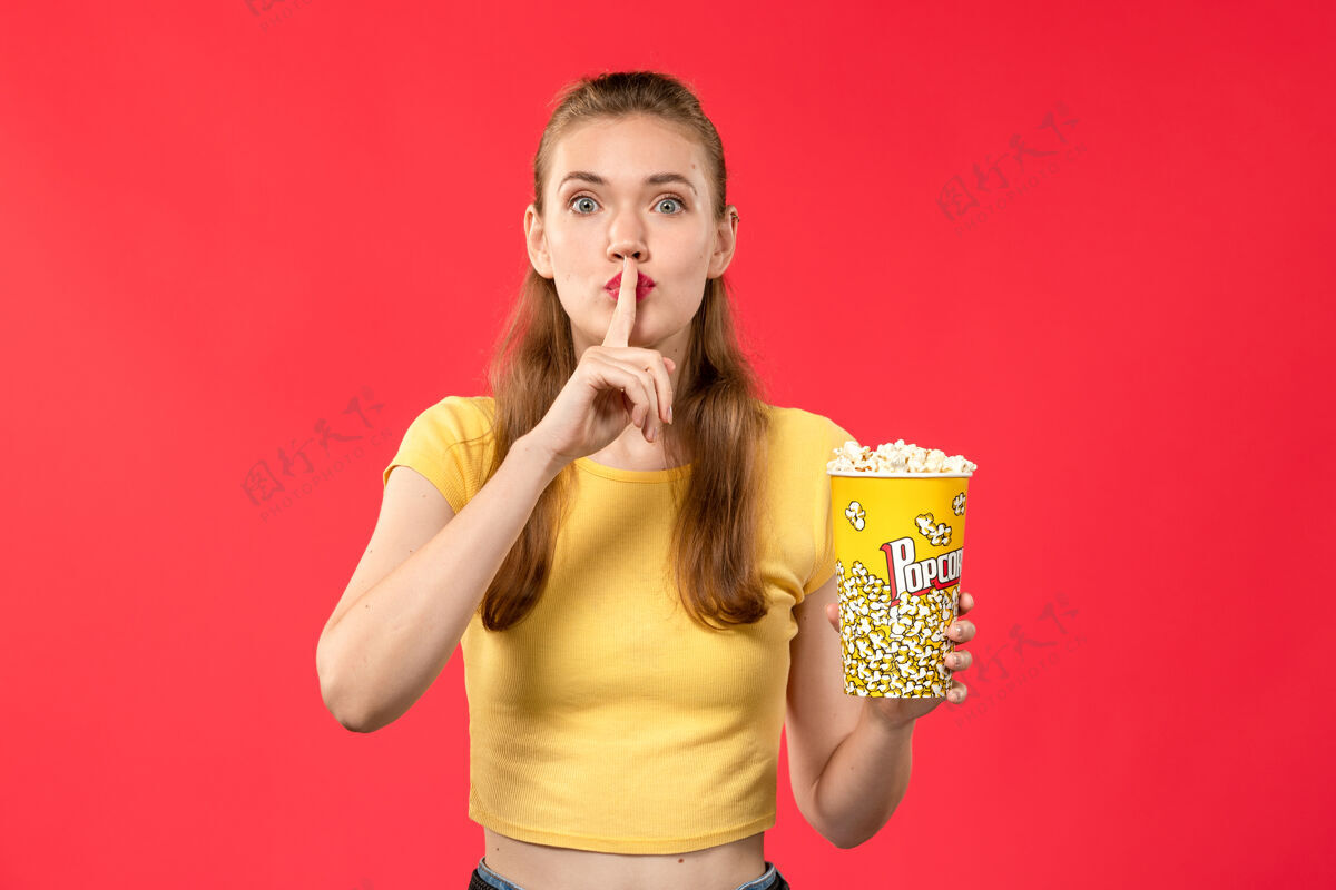 色彩正面图年轻女性在电影院里拿着爆米花 在红墙电影院摆着女性的姿势肖像表情艺人