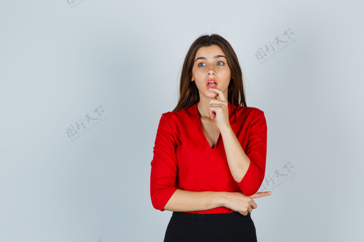 表情穿着红色上衣 裙子 手指放在嘴唇上的年轻女士看起来很困惑体贴困惑女人