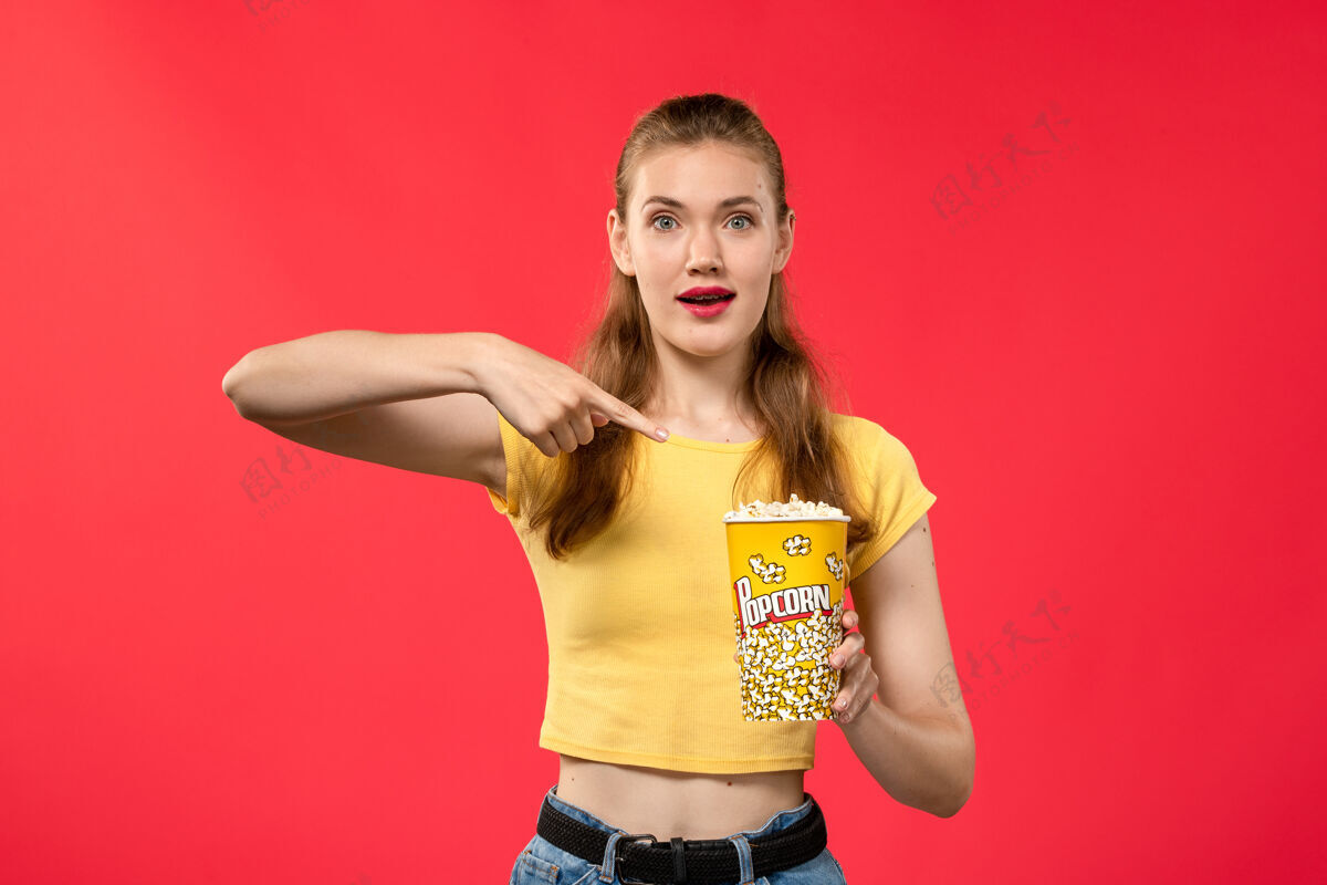 摆姿势正面图年轻女性在电影院拿着爆米花 在红墙电影院摆姿势 电影院小吃女性趣味电影电影美女电影