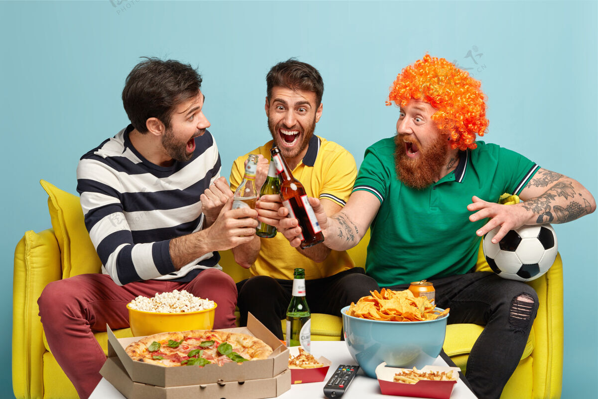 假发快乐的男人庆祝他们支持的足球队的胜利 碰杯啤酒 在家看体育比赛 吃零食 胜利地尖叫欣喜若狂的球迷在电视上享受全国比赛比赛支持小吃