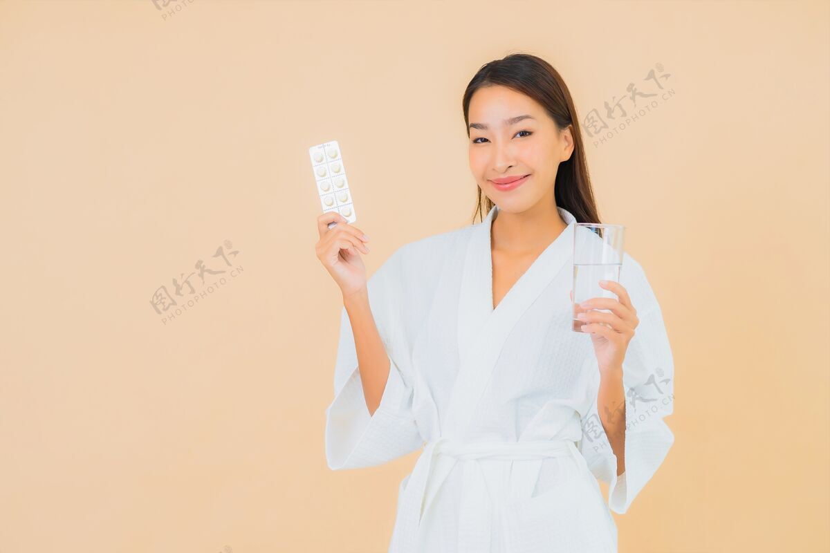 健康一幅美丽的亚洲年轻女子的画像 米色的水杯和药丸药丸医疗医药