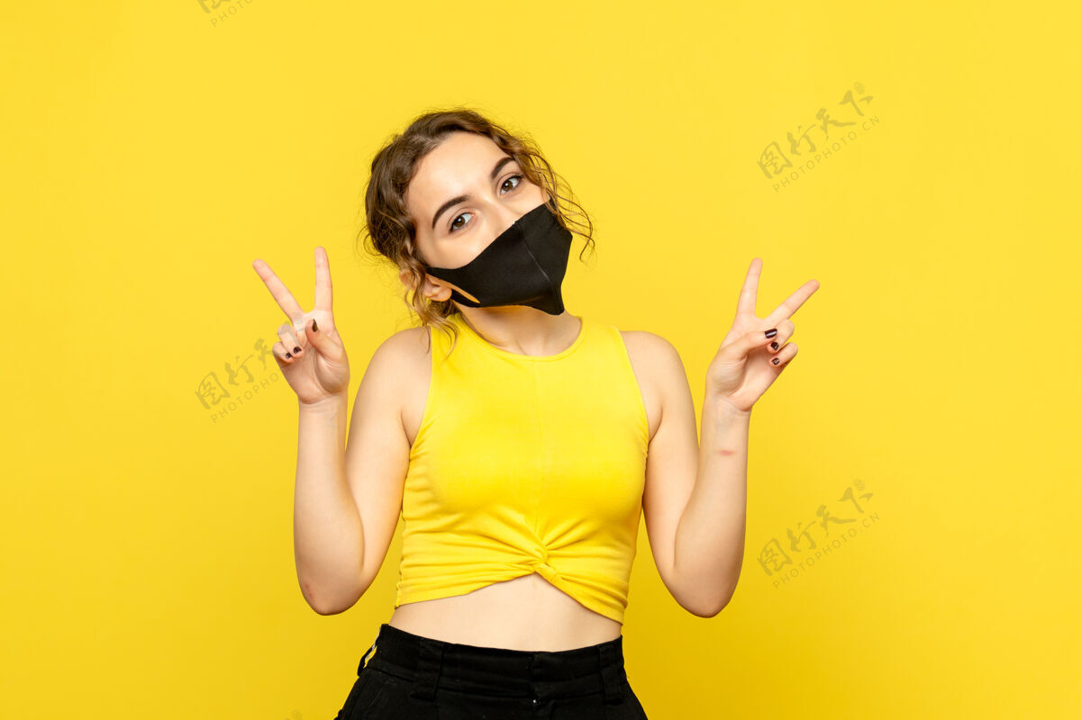 头发黄色墙壁上戴着黑色面具的年轻女子的正视图年轻姿势观点