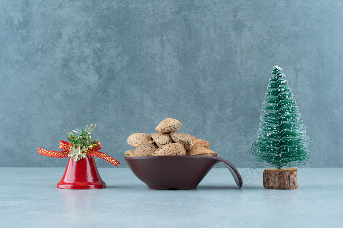 小雕像一碗去壳的杏仁和大理石上的圣诞装饰品有机圣诞树节日