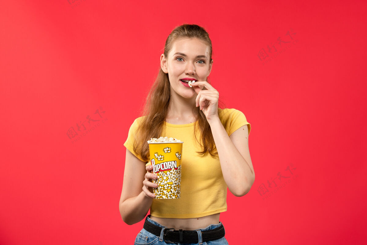 剧院前视图年轻女性在电影院拿着爆米花 在红墙电影院吃爆米花艺人年轻女性音乐家