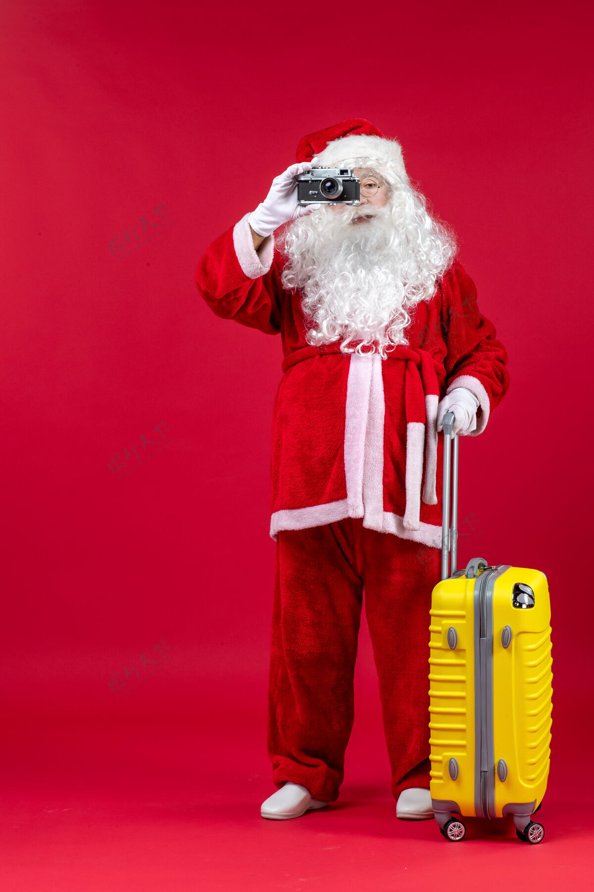 圣诞老人红墙上拿着相机的黄色袋子的圣诞老人的正视图男举行假期