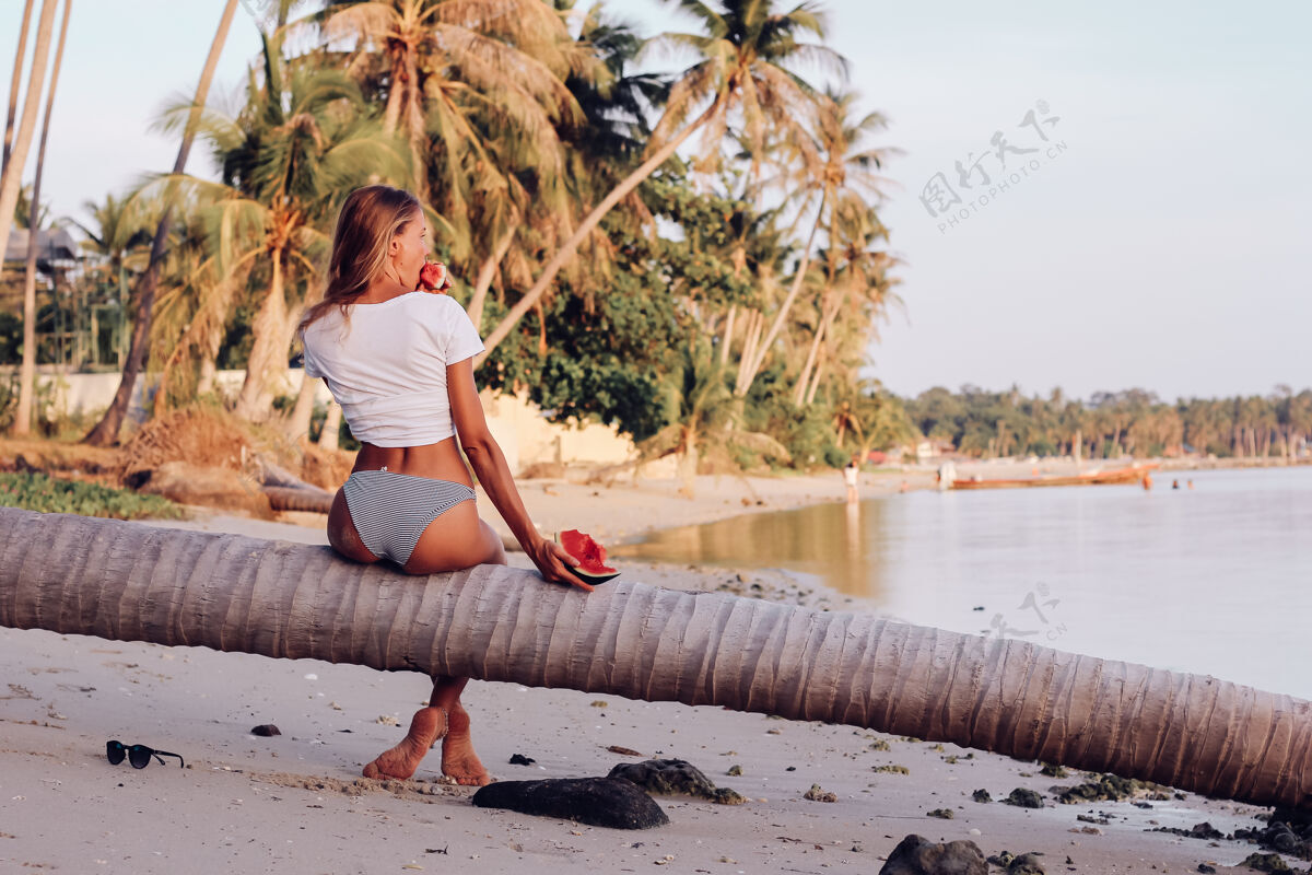 休息日落时分 在热带海滩上 一个年轻的女人拿着西瓜饮食西瓜美丽