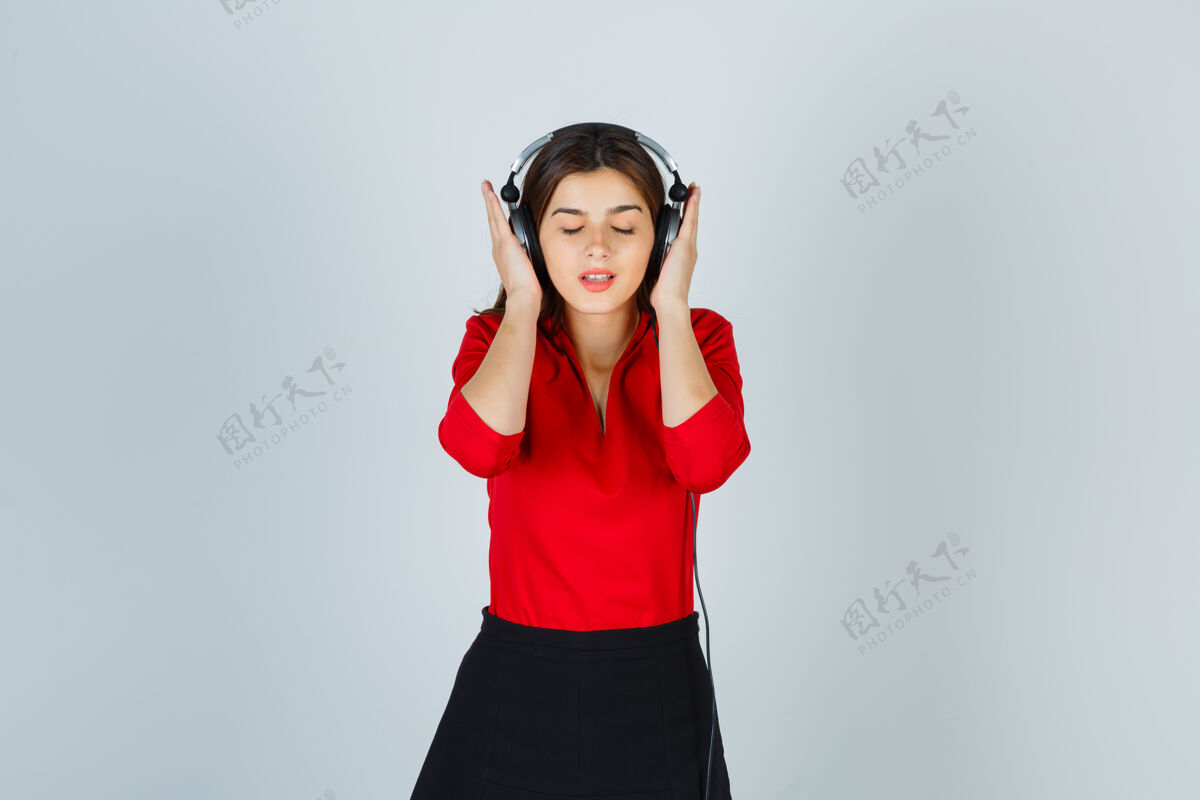 快乐戴着耳机的年轻女士穿着红色上衣 裙子听音乐 看上去很高兴多彩美丽快乐