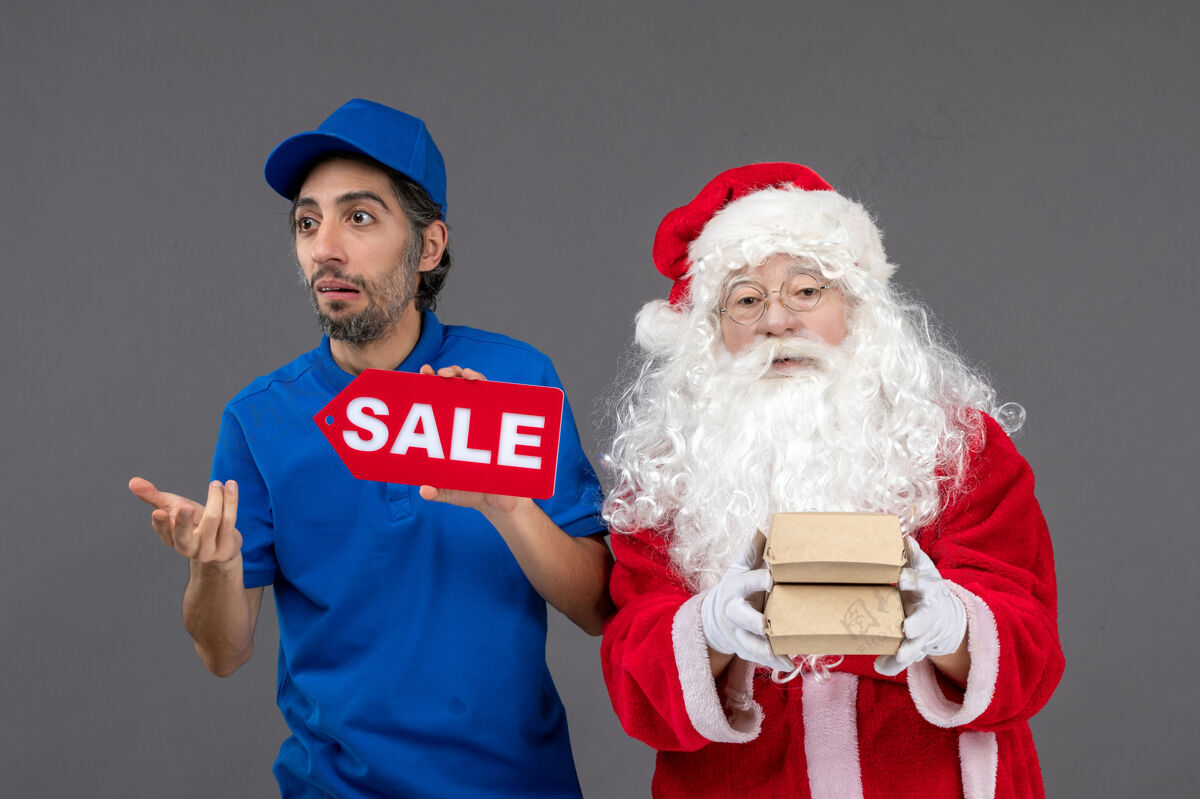 地板圣诞老人的正面图 男信使手持销售横幅 灰色墙上有食品包装男性正面快乐