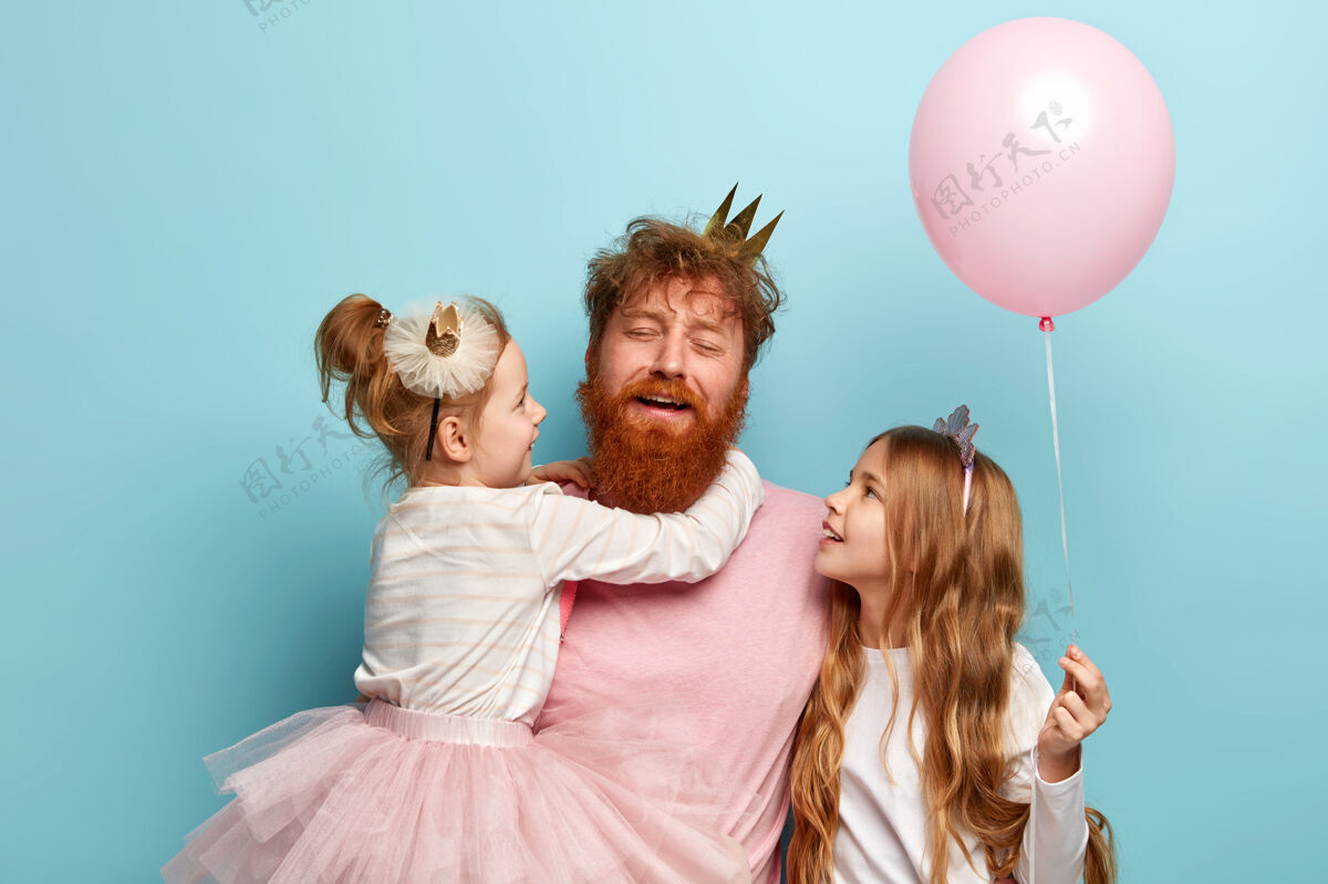 孩子横拍疲惫的年轻人 留着姜黄色的胡须 厌倦了和孩子们玩耍两个女儿和深情的爸爸一起度假 捧着粉色的气球节日概念童年积极满足