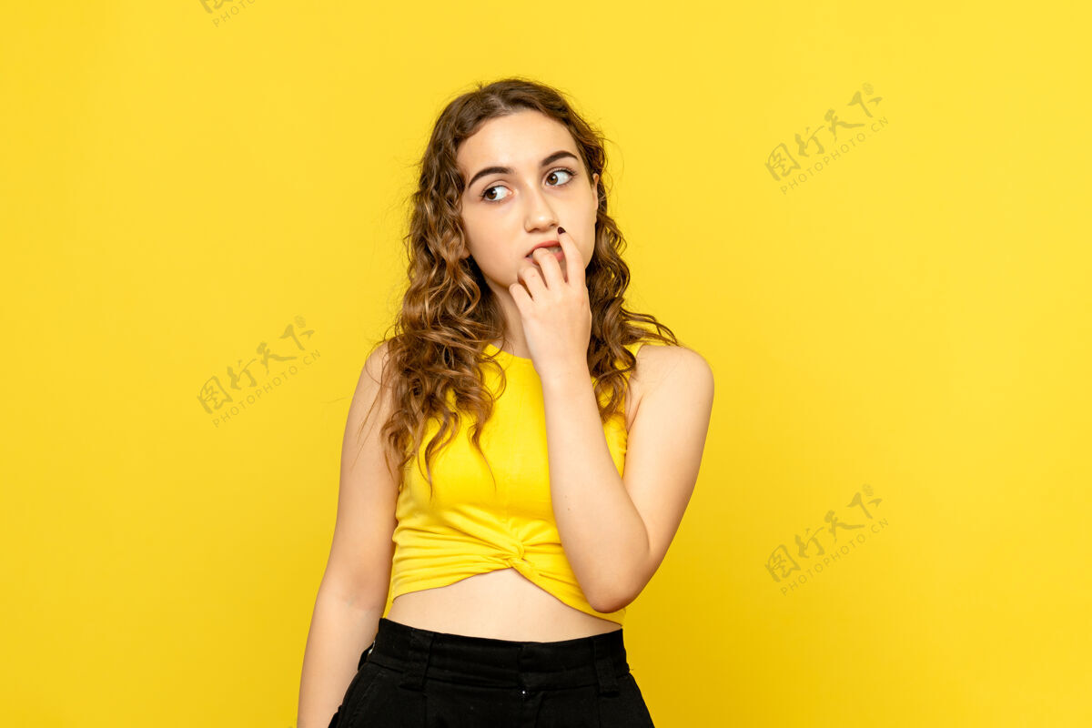 年轻女性年轻女子在黄墙上思考的正面图女性时尚模型