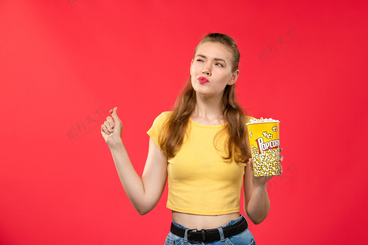 电影正面图年轻女性在电影院拿着爆米花 带着思考的表情在红墙电影院看女性趣味电影电影漂亮表达