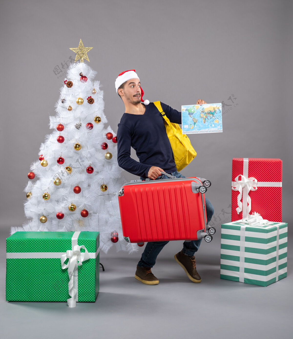 圣诞树一个带着黄色背包的年轻人拿着圣诞树旁的地图 礼物是灰色的附近帽子圣诞老人