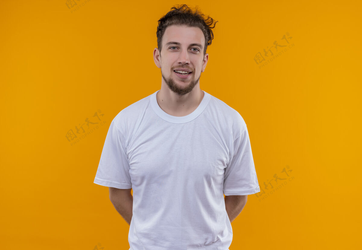 橙色微笑的年轻人穿着白色t恤 把他的手放在孤立的橙色背景上T恤微笑年轻