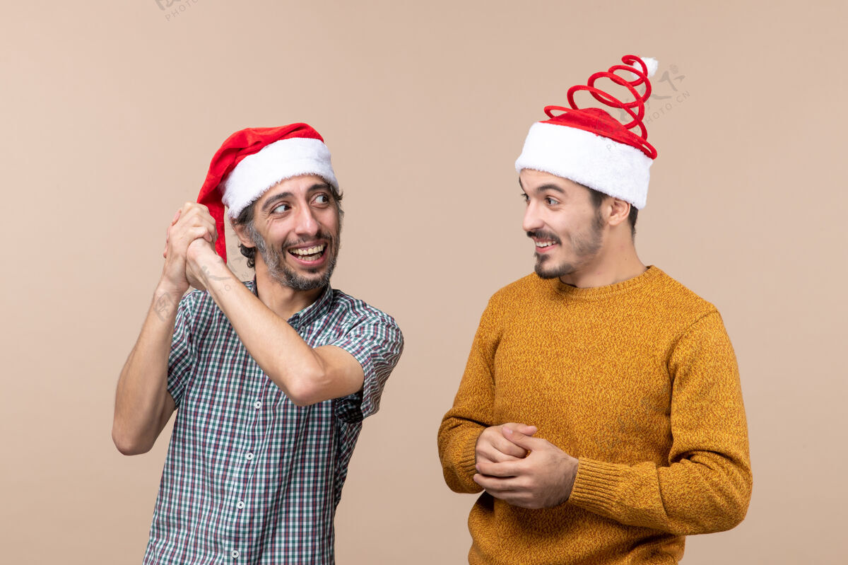 微笑正面图两个带着圣诞帽的微笑的家伙在米色孤立的背景下看着对方米色风景两个
