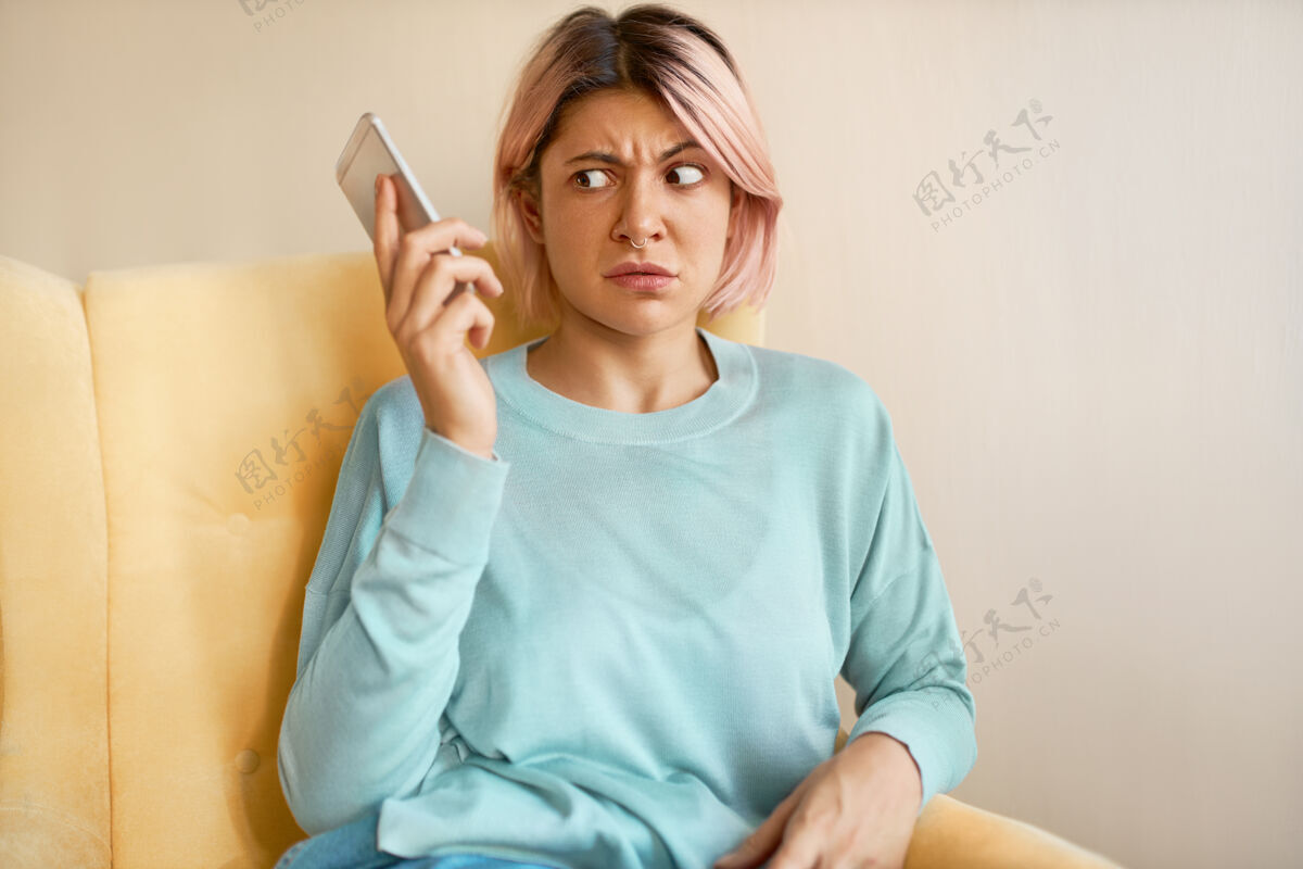 通话一个皱眉的穿着蓝色运动衫的年轻女子拿着手机 拨错了号码 一副震惊的样子手机房子电话