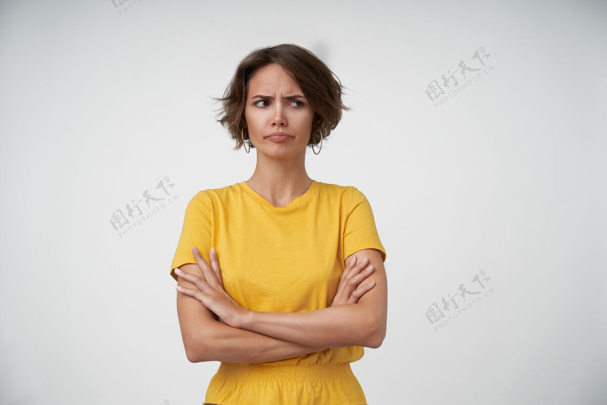 发型一幅年轻的黑发女子的肖像 随意的发型 眉头紧锁 双手交叉放在胸前 站着的时候穿着黄色t恤折叠女性美丽